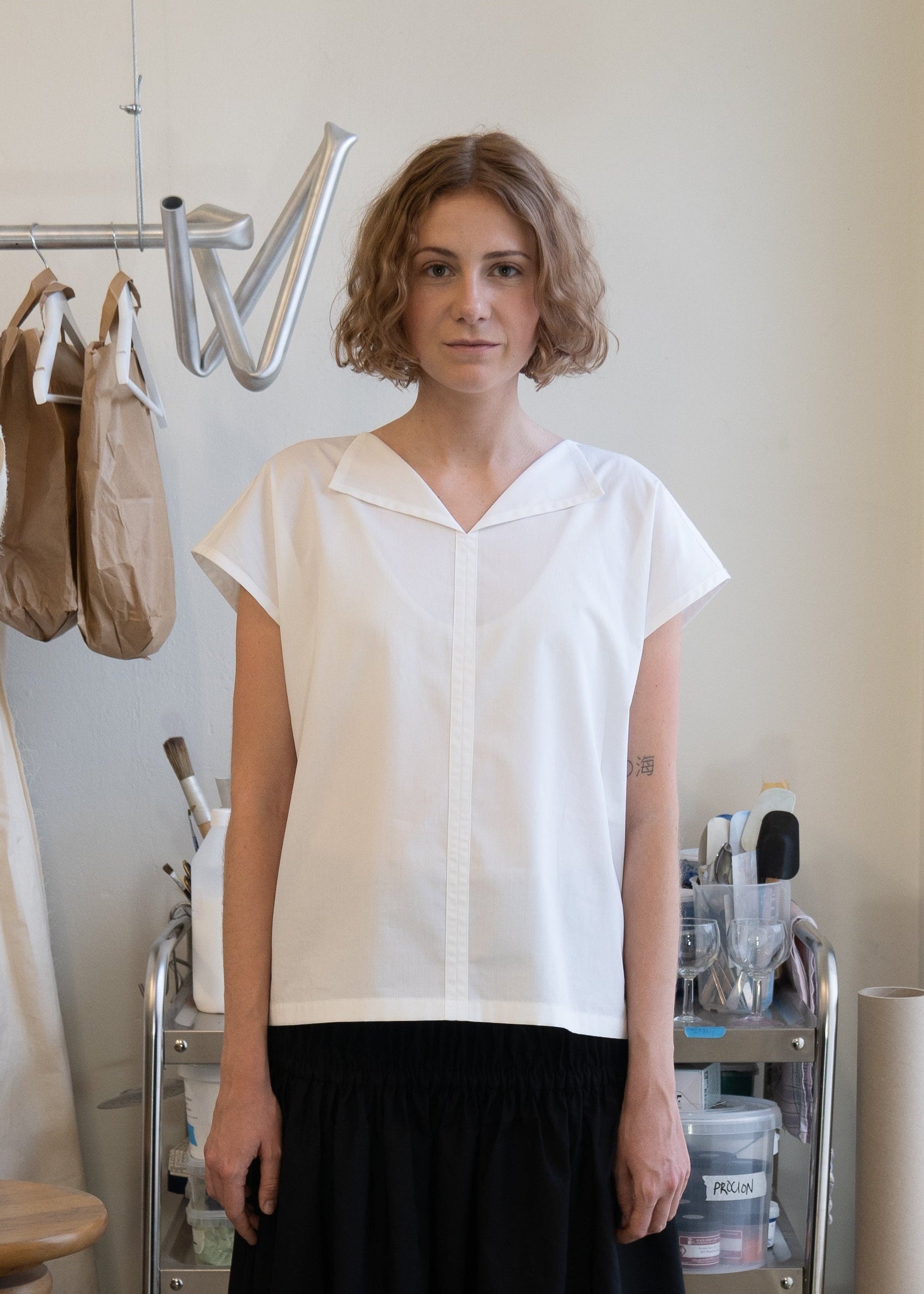 Woman standing in a clothing store wearing a white blouse and black skirt.