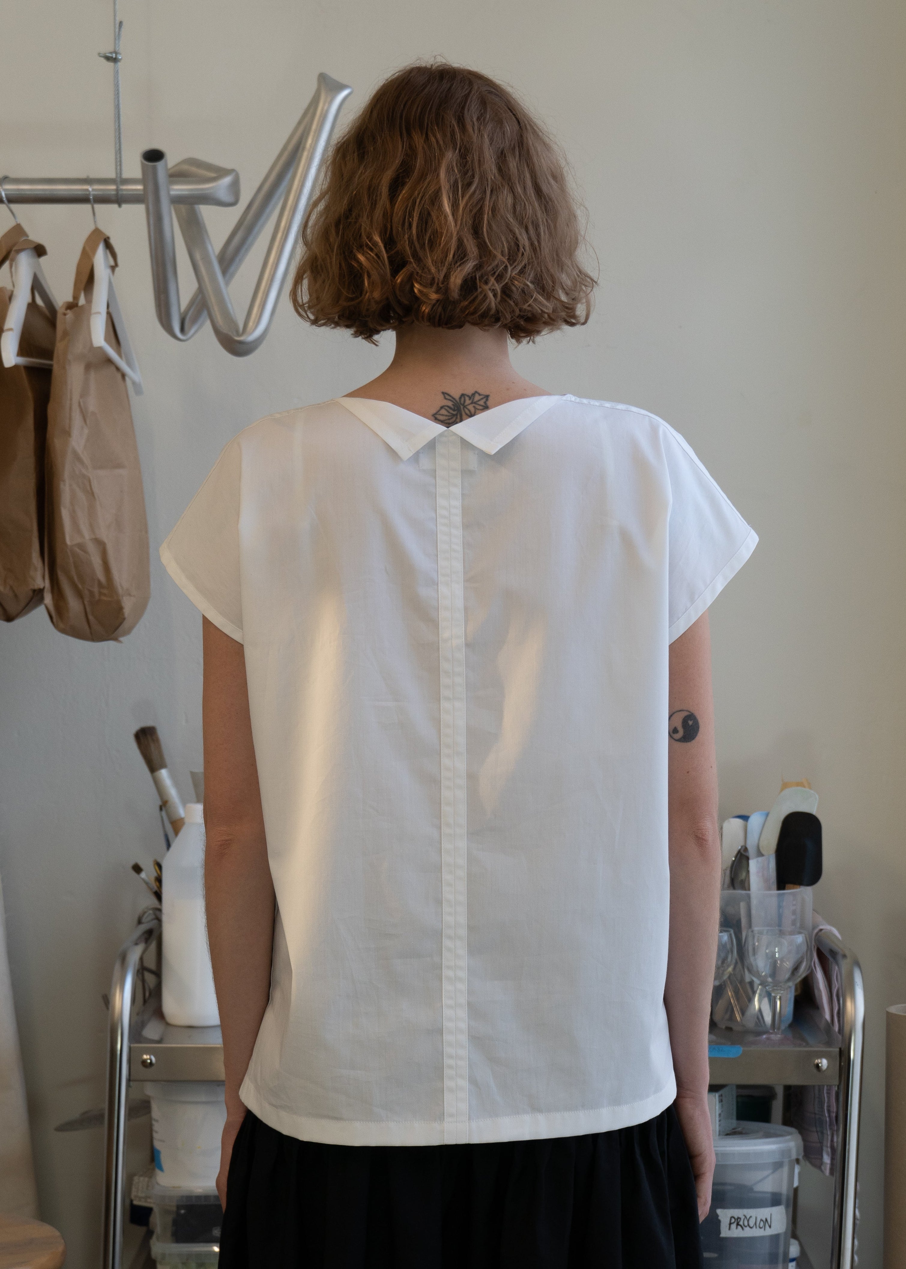 Person wearing a white blouse with a visible back design in a casual setting.