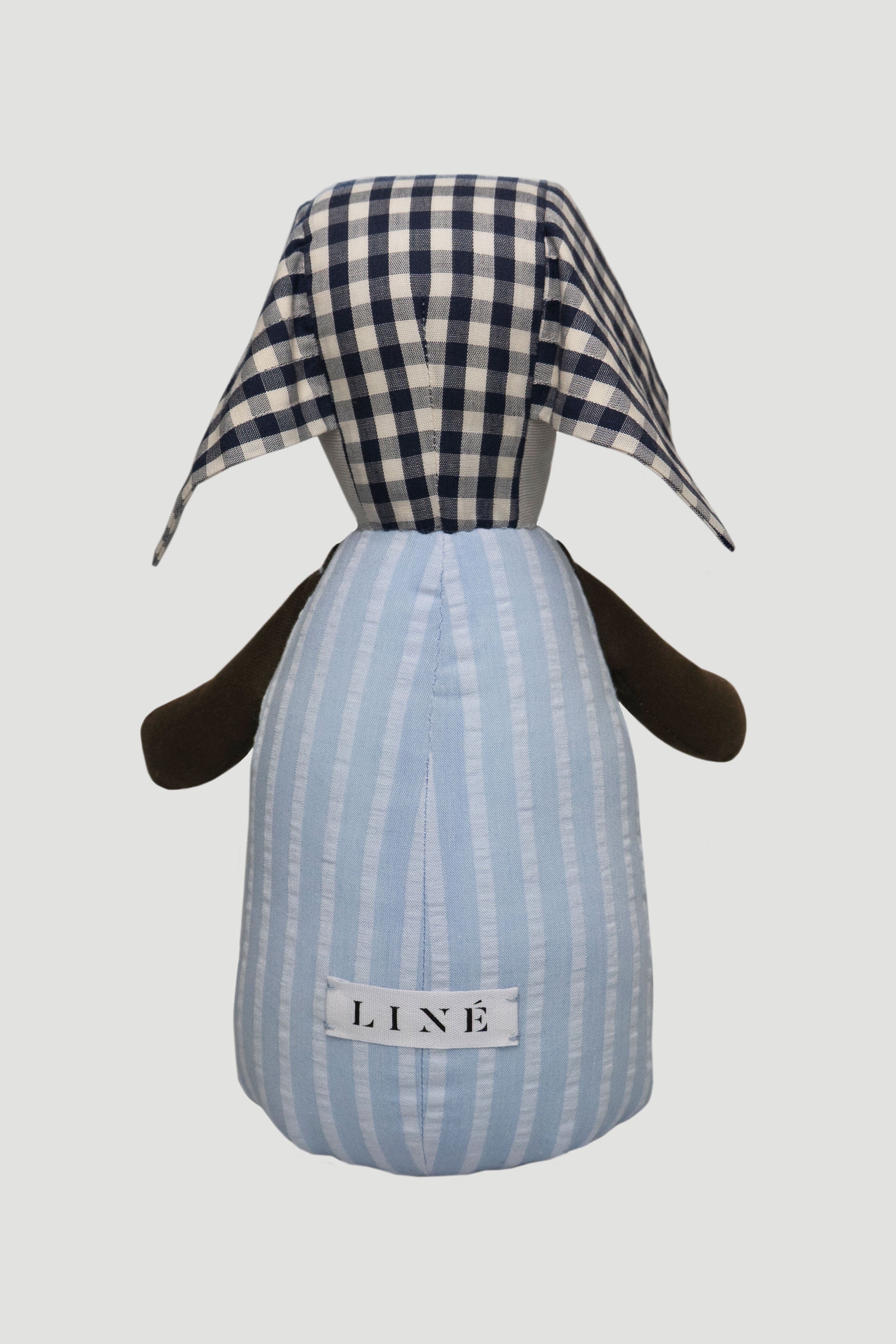 Teddy toy with checkered ears, striped blue body and brown arms seen from the back