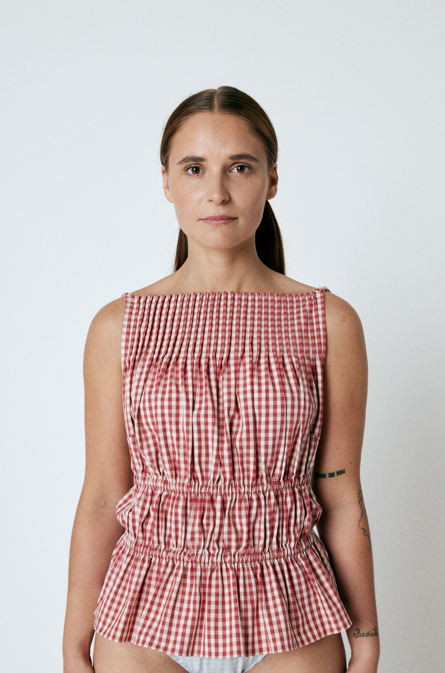  LINÉ Pintuck Top Red. Pintucks at neckline · Elastic shoulder straps · Elastic casing under the bust and around the waist · Low back · The back hem is slightly elongated and is separated from the front by a small slit in the side seams · Model is 162 cm and wears size 1 · Made-to-order · Produced locally in Denmark · Material: 100 % organic cotton yarn dyed gingham · Collection: Gingham Garments. LINÉ