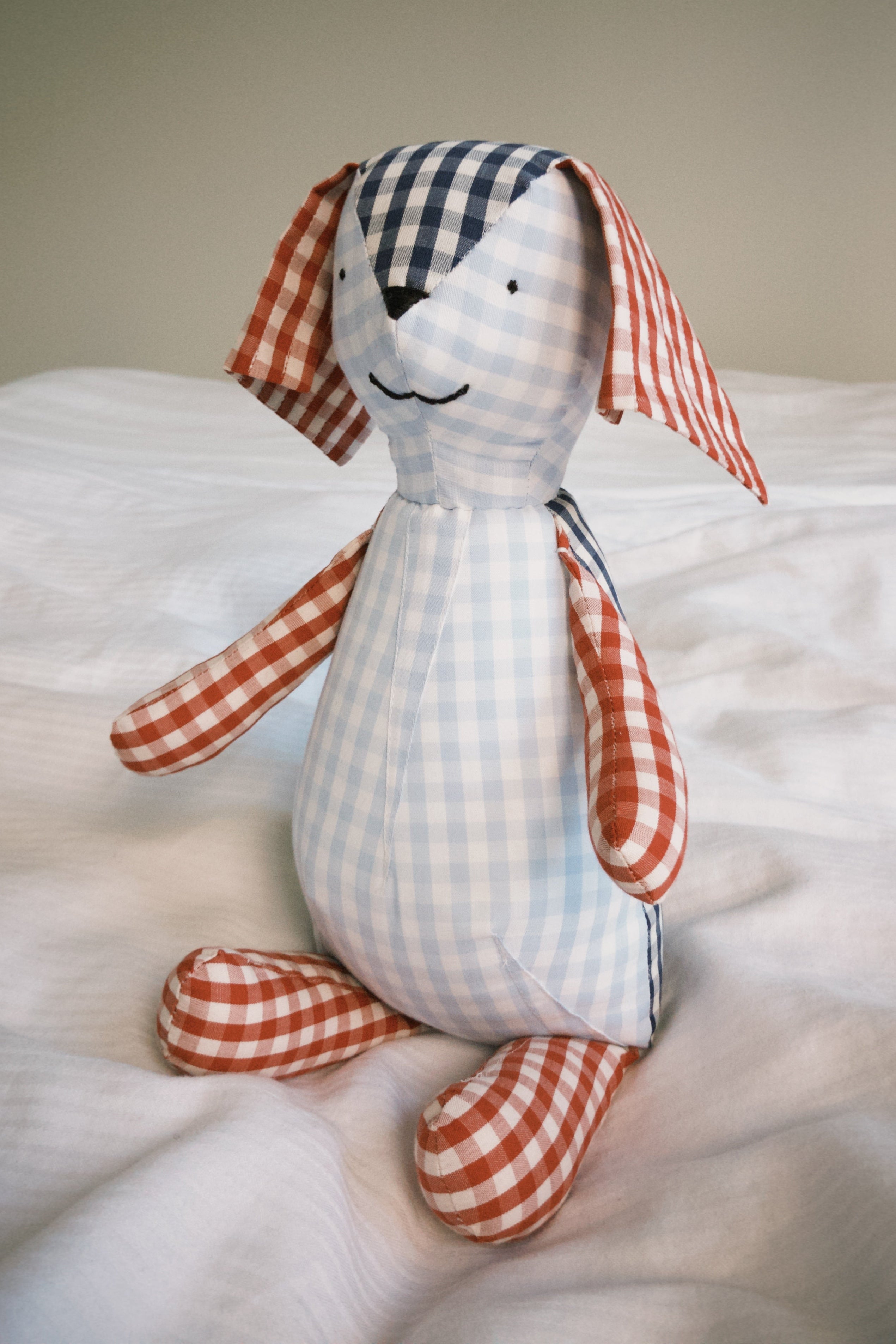 Stuffed teddy toy with checkered pattern sitting on a bed