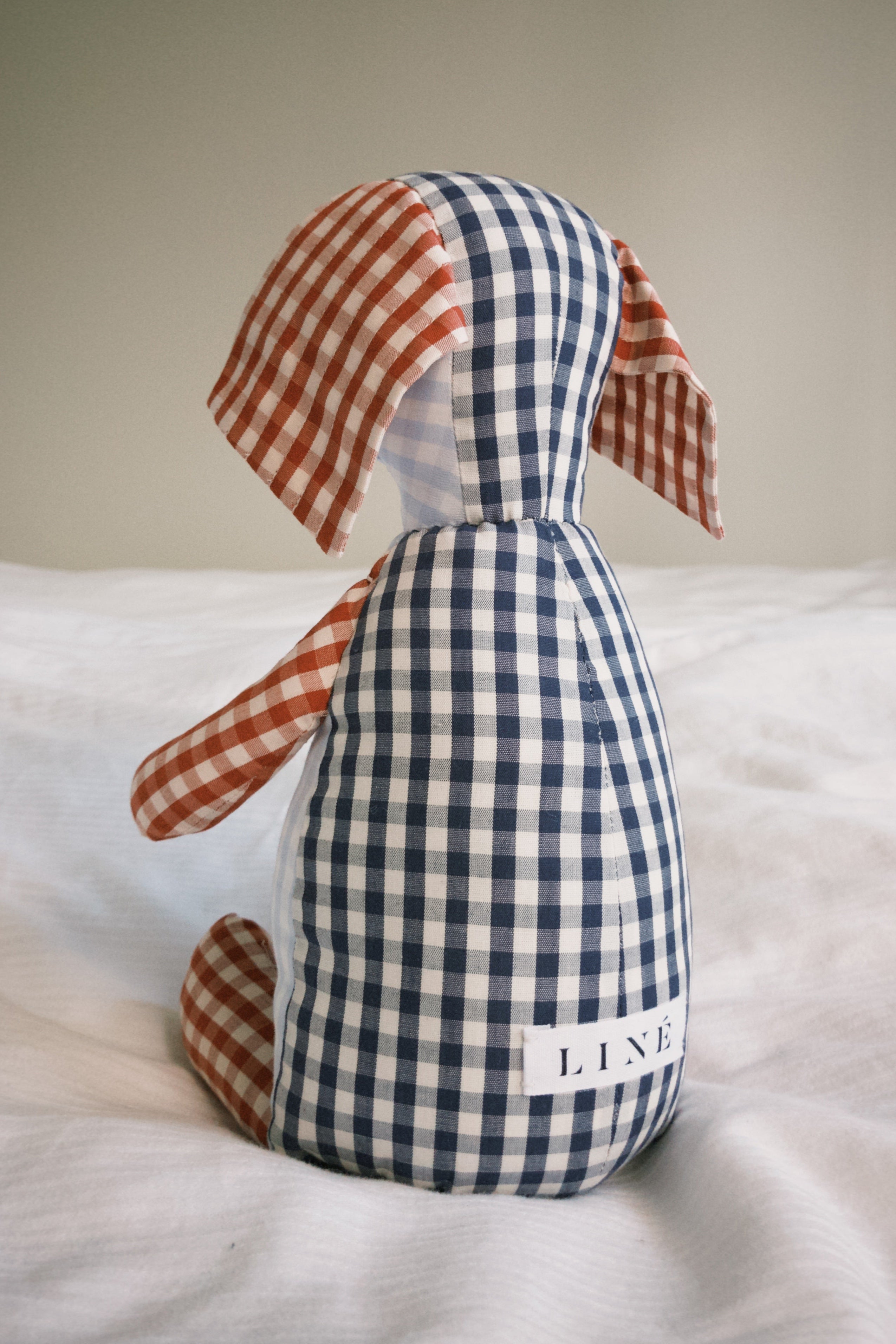 Stuffed teddy toy with blue and white checkered pattern sitting on a bed