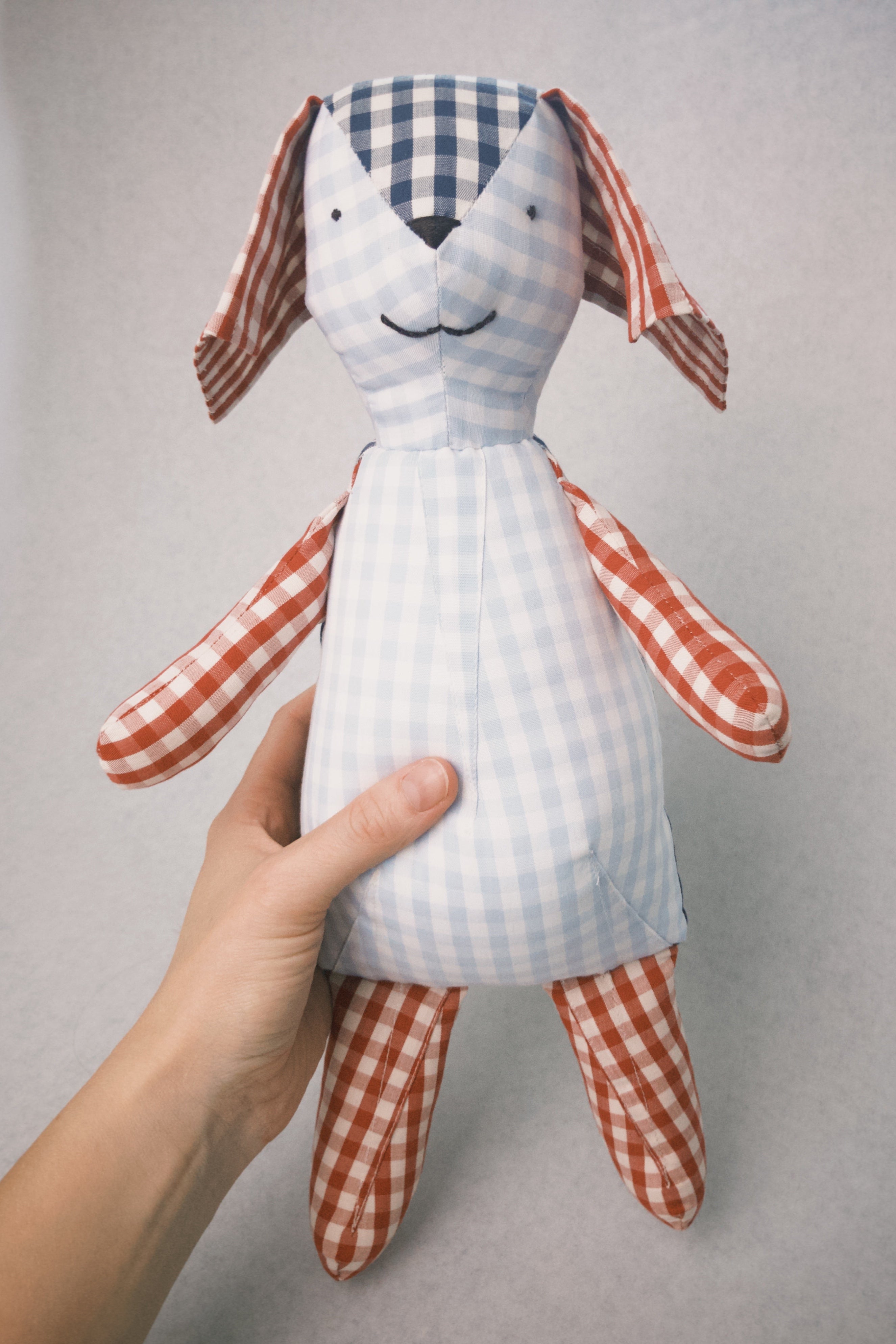 Hand holding a teddy toy with checkered pattern against a plain background